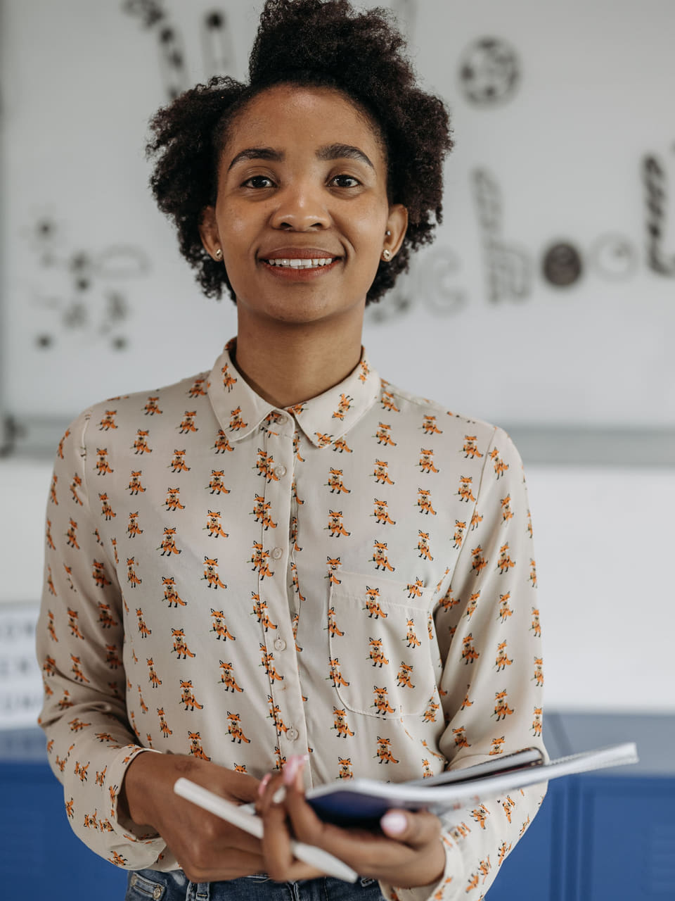 A teacher holding a notebook in front of a classroom wall